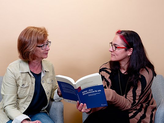 Zwei Personen sitzen nebeneinander und eine Person hat ein Buch in der Hand