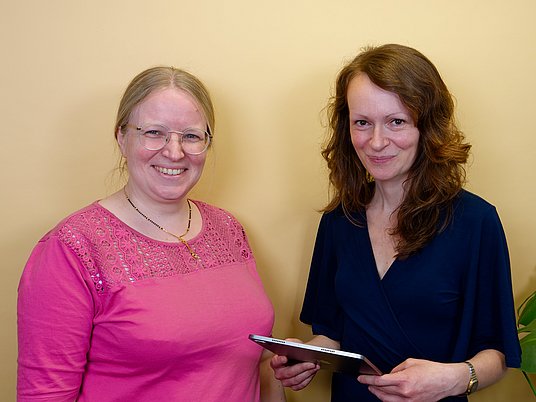 Zwei Personen stehen nebeneinander und eine hat ein Buch in der Hand