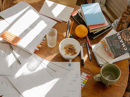 Auf einem Tisch liegen durcheinander Unterlagen, Bücher, Geschirr und Essen 